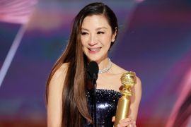 Michelle Yeoh, in a black evening gown, holds her Golden Globe on stage. She looks happy.