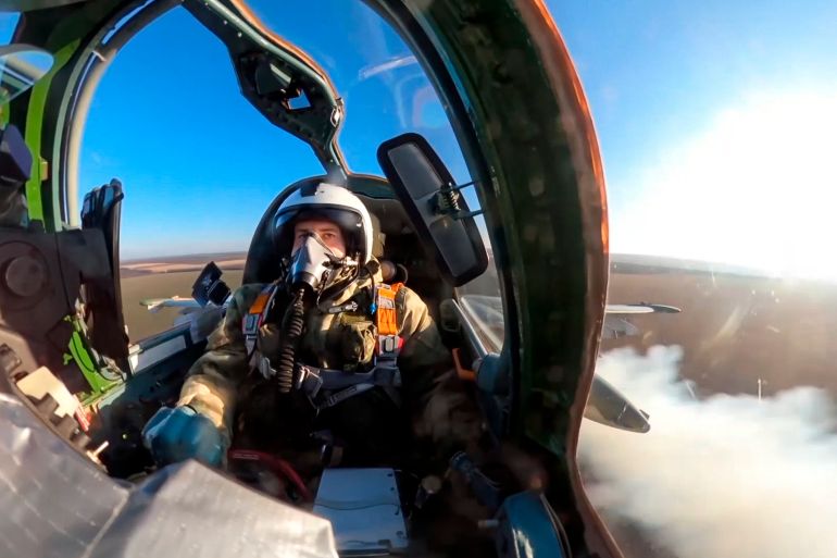 An image from inside the cockpit showing a Russian pilot of an SU-25 in the air. There is blue sky and some clouds and the earth below.
