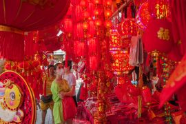 A woman shopping for Lunar New Year decorations in Jakarta's Chinatown. She is in line green and the stalls around her are decked out in red lanterns