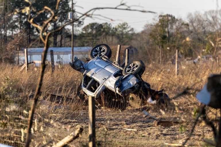 An overturned and destroyed SUV near a county road. It is lying among dry grass and twigs