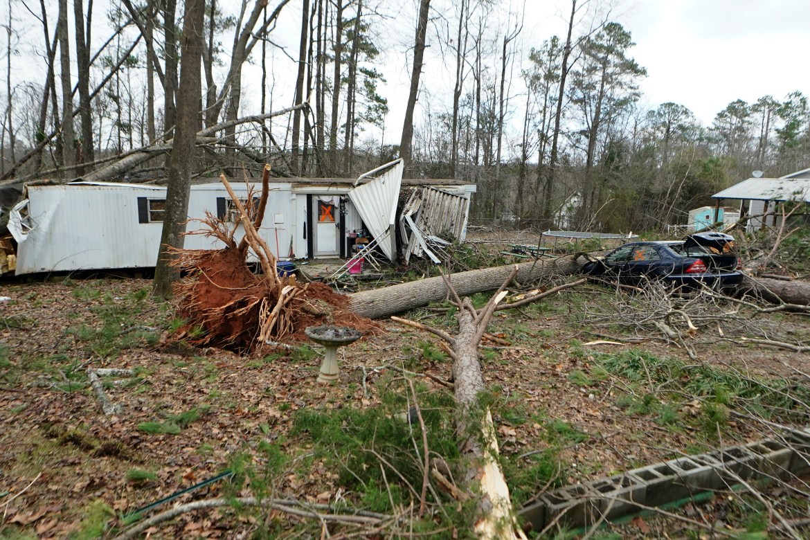 A mobile home sits next to a fallen tree