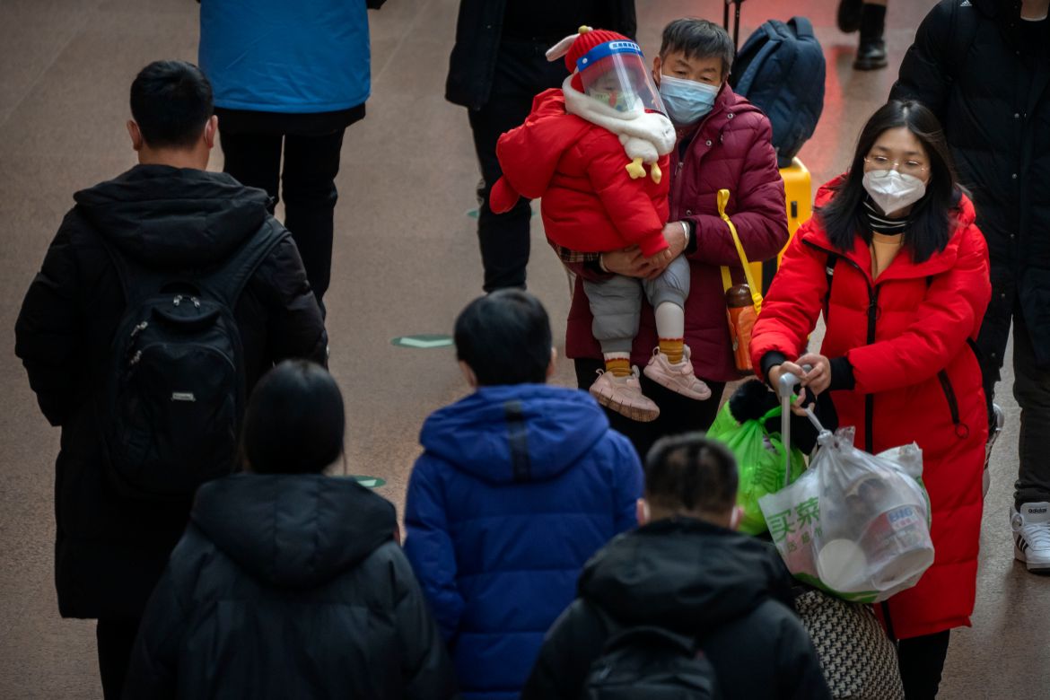 A woman carries a child wearing a face mask and face shield as they walk along a concourse at Beijing West Railway Station in Beijing