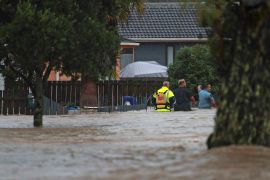 Emergency workers and a man wade through flood waters in Auckland, New Zealand