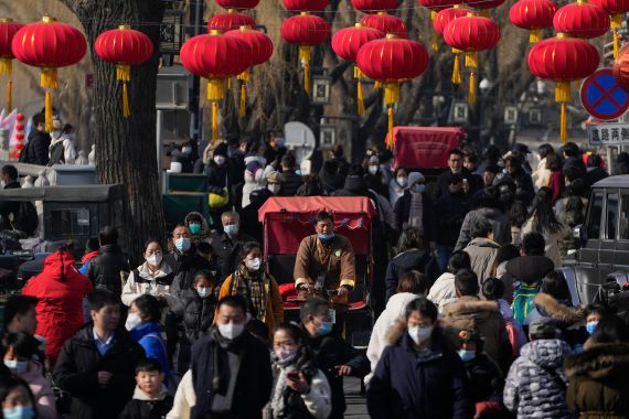 People in China walk beneath a row of red lanterns in Beijing, China. The street is very crowded.