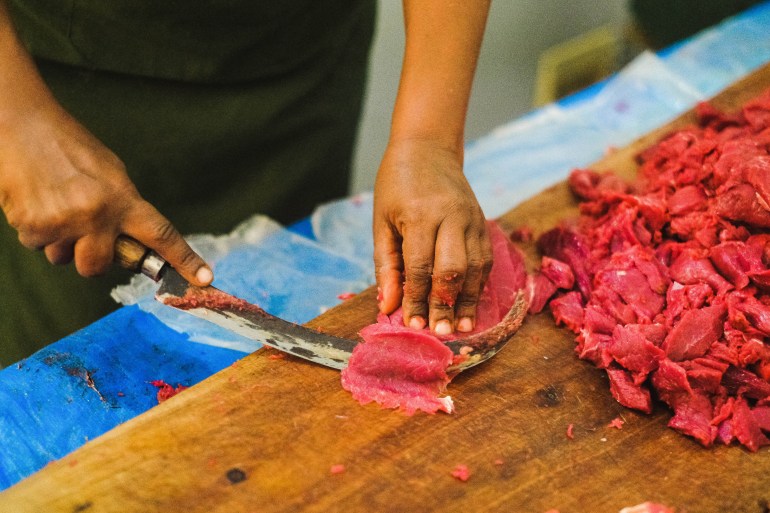 A photo of a cooks hands as she cleans the red meat for kitfo, using a special curved knife