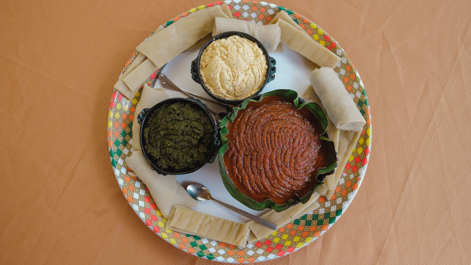 A final tray for a customer with a bowl of kitfo, gomen kitfo, and ayeb, surrounded by kocho and rolls of injera