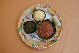 A final tray for a customer with a bowl of kitfo, gomen kitfo, and ayeb, surrounded by kocho and rolls of injera