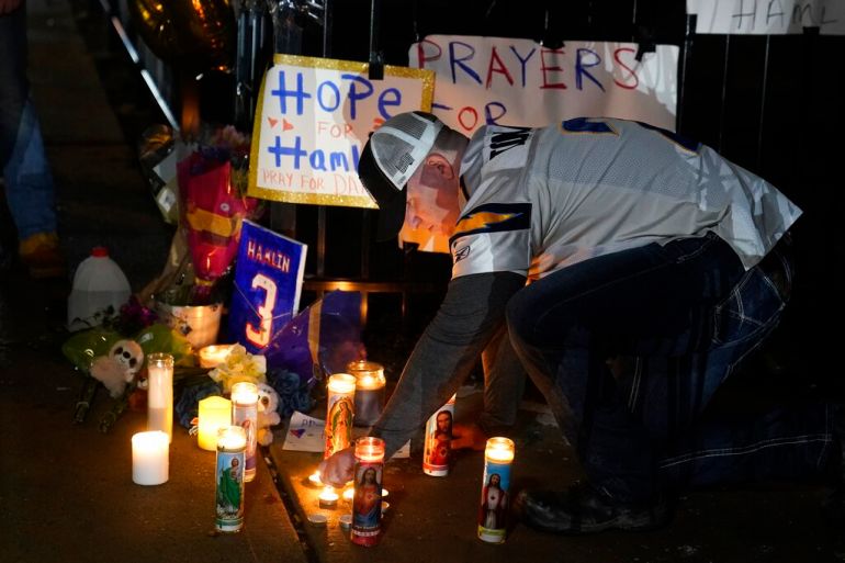 A man lights a candle surrounded signs of support for Hamlin