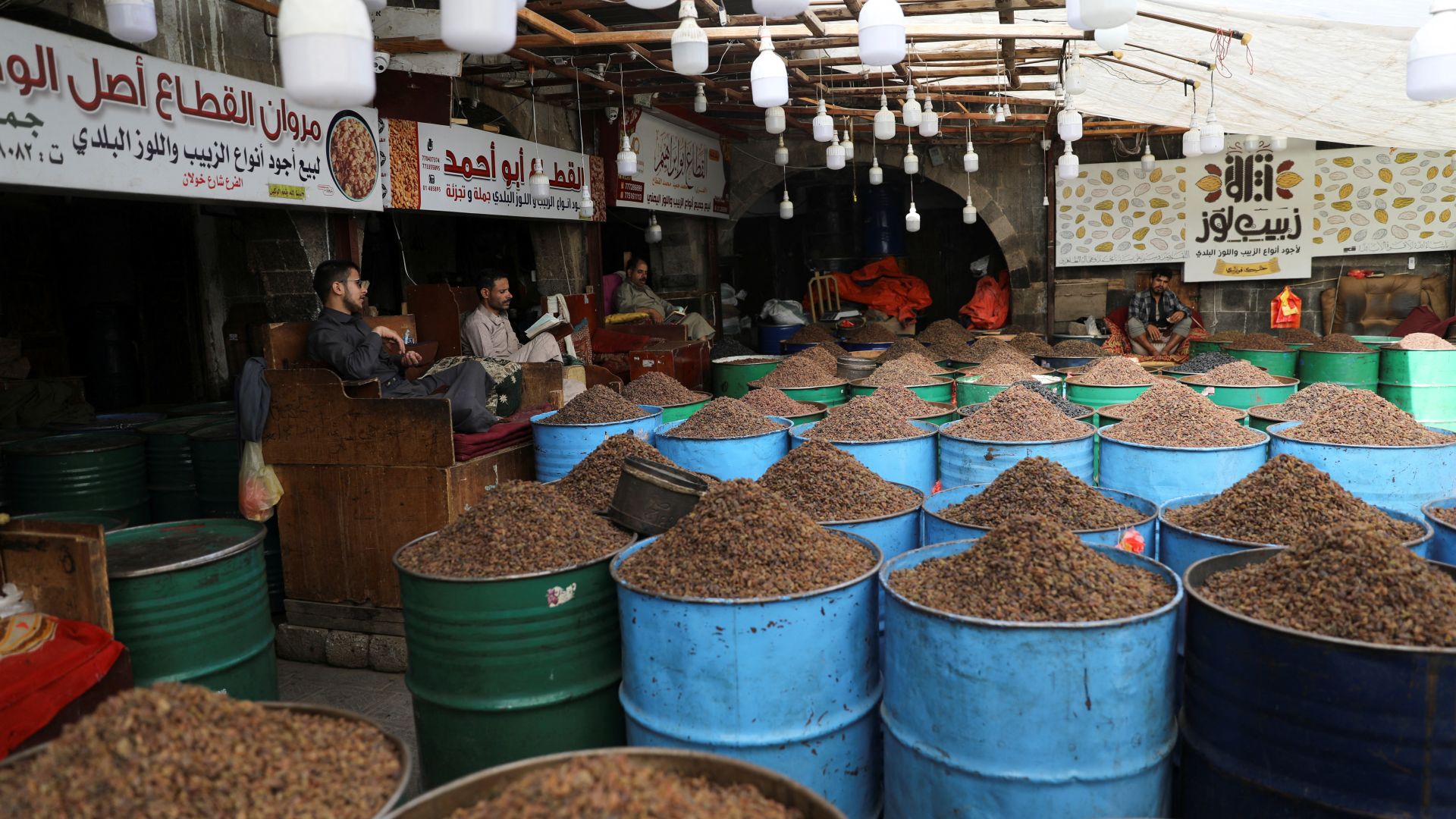 A photo of a market with barrels of raisins and people sitting in chairs behind the barrels.