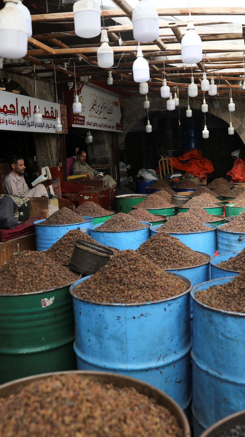 A photo of a market with barrels of raisins and people sitting in chairs behind the barrels.