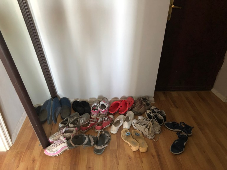 A photo of several pairs of shoes and slippers by a wall.
