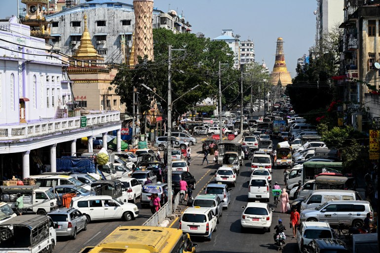 A busy street in Yangon showing cars filling the streets in each direction. The golden stupa of the Sule Pagoda is behind