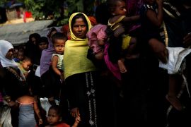 Rohingya women and children queuing up for food supplies at a refugee camp in Bangladesh. They are carrying bags and buckets.