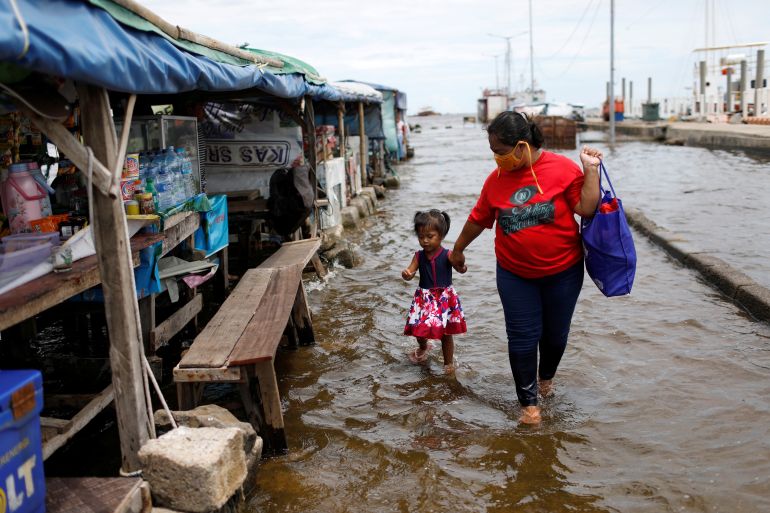 Evi, a 35-years-old vendor, walks with her 2-years-old daughter through water at Kali Adem port, which is impacted by high tides due to the rising sea level and land subsidence, north of Jakarta, Indonesia November 20, 2020. REUTERS/Willy Kurniawan
