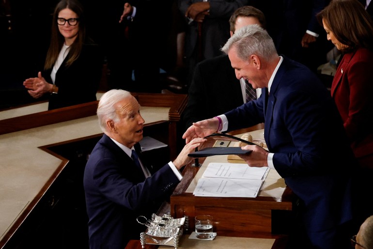 Biden shakes McCarthy's hand. McCarthy looks down smiling at Biden. 
