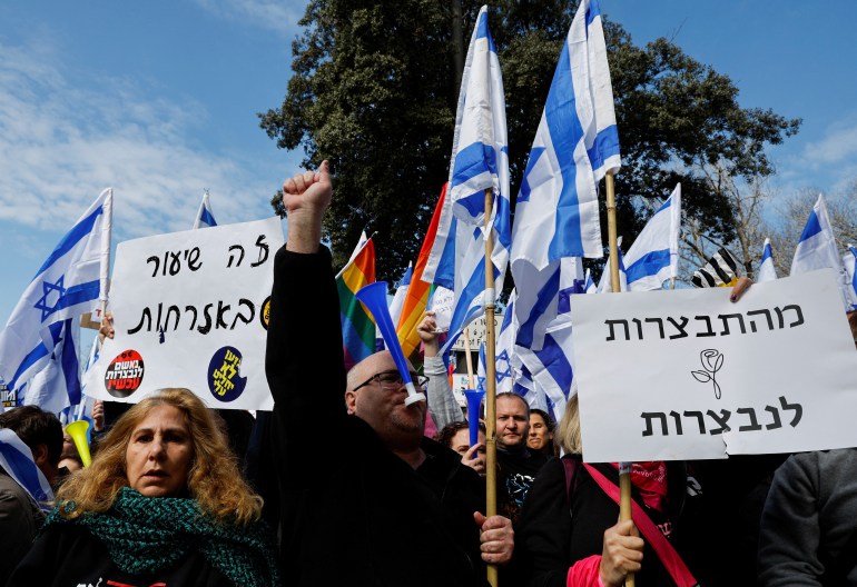 Israelis hold flags and posters as they demonstrate on the day Israel's constitution committee is set to start voting on changes that would give politicians more power on selecting judges while limiting Supreme Court's powers to strike down legislation, outside the Knesset, Israel's parliament in Jerusalem, February 13, 2023.
