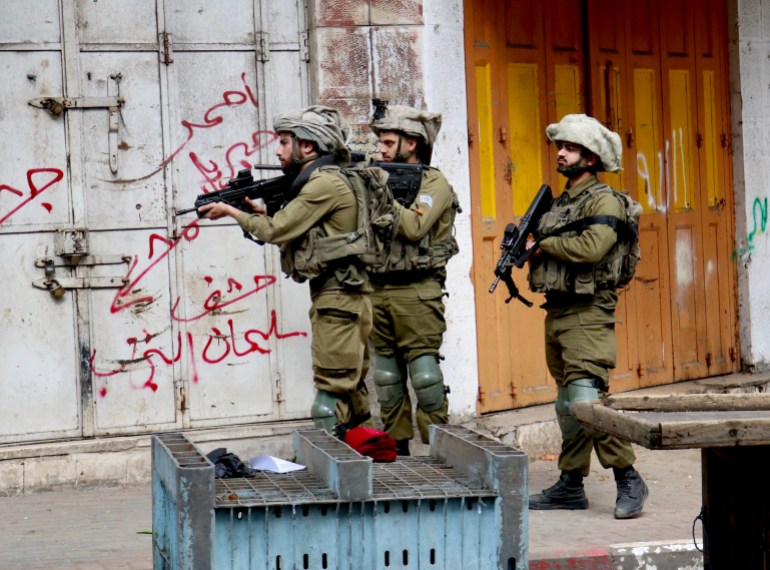 Three Israeli soldiers, holding their guns, in confrontations with marching Palestinians