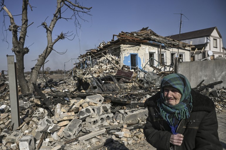 An eldery woman stands in front of a destroyed house after bombardments in the village of Krasylivka, east of Kyiv