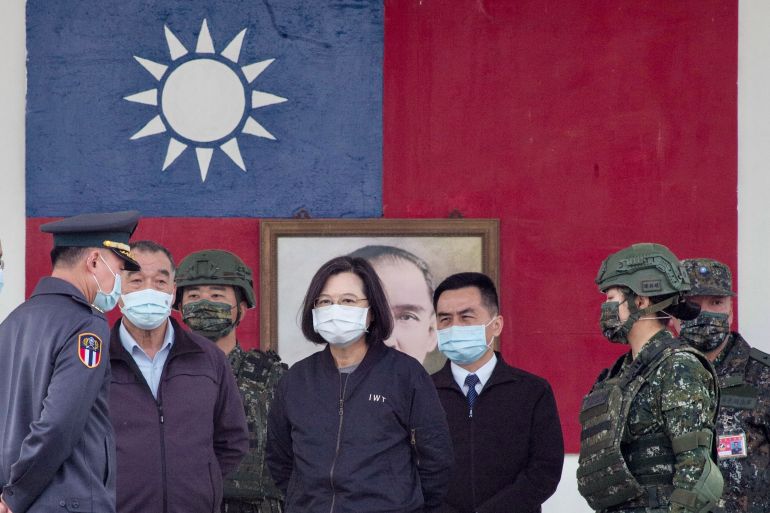 Taiwan President Tsai Ing-wen standing with military and civilian officials at a military base in Chiayi. There is a large Taiwan flag behind them