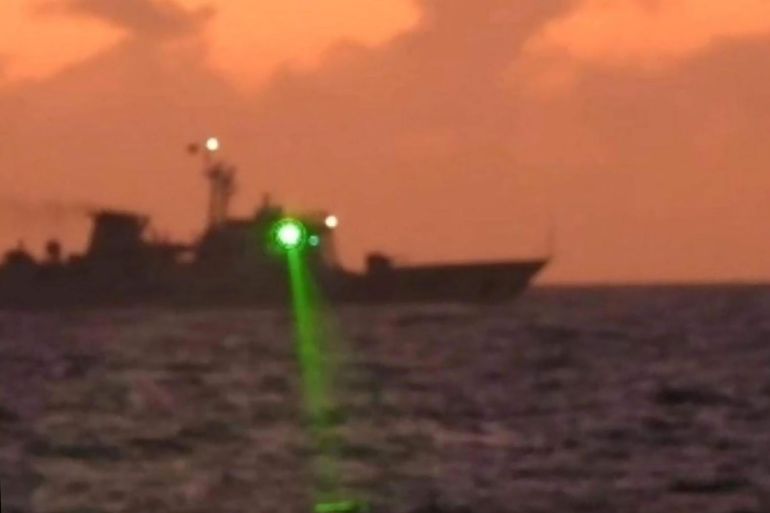 A photo showing a green light being directed from a ship. The vessel is silhouetted against an orangey sky