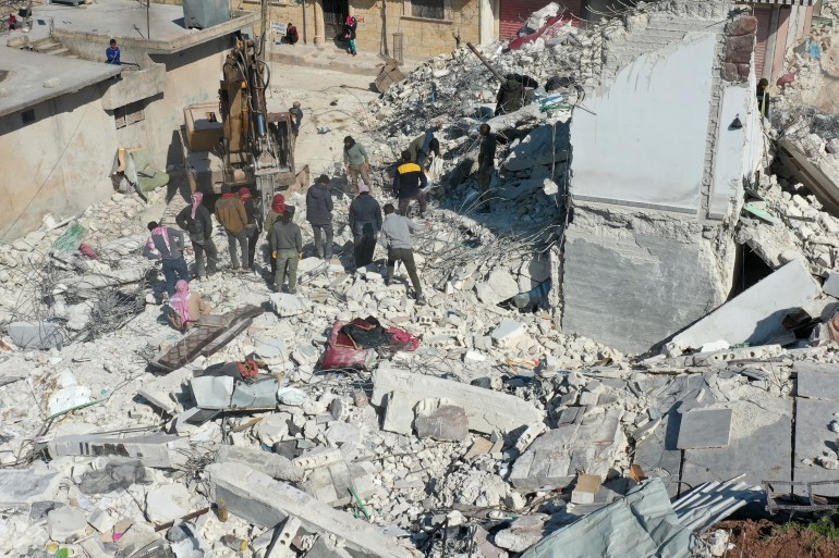 An aerial view shows a digger working on the rubble of a collapsed building in the Syrian rebel-held town of Jindayris on February 15, 2023, following the February 6 earthquake that hit Turkey and Syria. - The 7.8-magnitude earthquake has killed at least 40,000 people and devastated swathes of Syria and neighbouring Turkey. (Photo by Omar HAJ KADOUR / AFP)