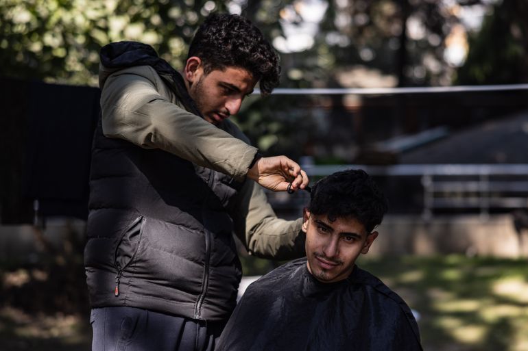Eighteen-year-old Syrian Mohammed al-Hamo (L) cuts the hair of his 19-year-old brother Sobhi (R) in front of their tent at a makeshift camp in the city of Antakya on February 19, 2023. - A 7.8-magnitude earthquake hit near Gaziantep, Turkey, in the early hours of February 6, followed by another 7.5-magnitude tremor just after midday. The quakes caused widespread destruction in southern Turkey and northern Syria and has killed more than 44,000 people.