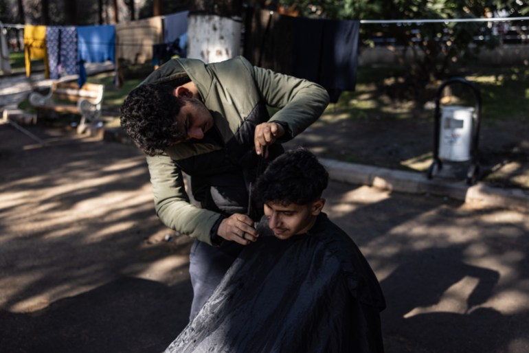 Eighteen-year-old Syrian Mohammed al-Hamo (L) cuts the hair of his 19-year-old brother Sobhi (R) in front of their tent at a makeshift camp in the city of Antakya on February 19, 2023. - A 7.8-magnitude earthquake hit near Gaziantep, Turkey, in the early hours of February 6