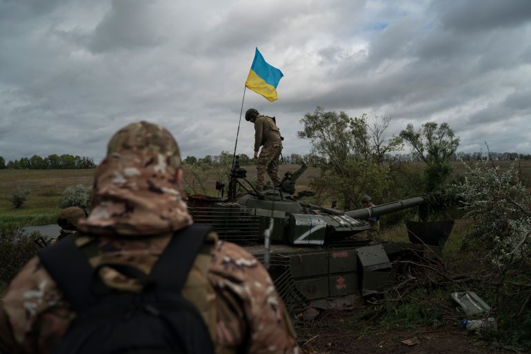 A Ukrainian soldier stands atop a destroyed Russian tank