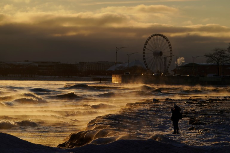 A person stands on a dimly lit shore of Lake Michigan on Friday, with the ferris wheel from Chicago's Navy Pier in the background