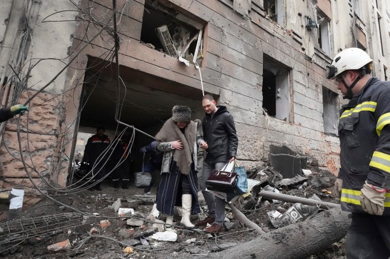 A man helps a lady to walk out from a residential building in Kharkiv