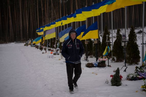 A man walks through a cemetery with Ukrainian flags in a row behind him.