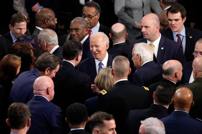 Biden is smiling as he talks to a legislator. They are surrounded by many heads, mostly of men
