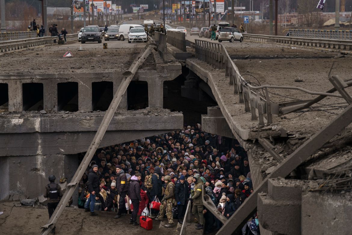 Ukrainians crowd under a destroyed bridge as they try to flee by crossing the Irpin River on the outskirts of Kyiv