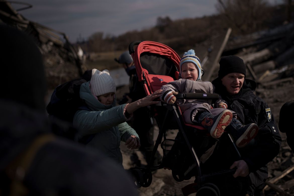 A child in a stroller is lifted across an improvised path as people flee Irpin, on the outskirts of Kyiv