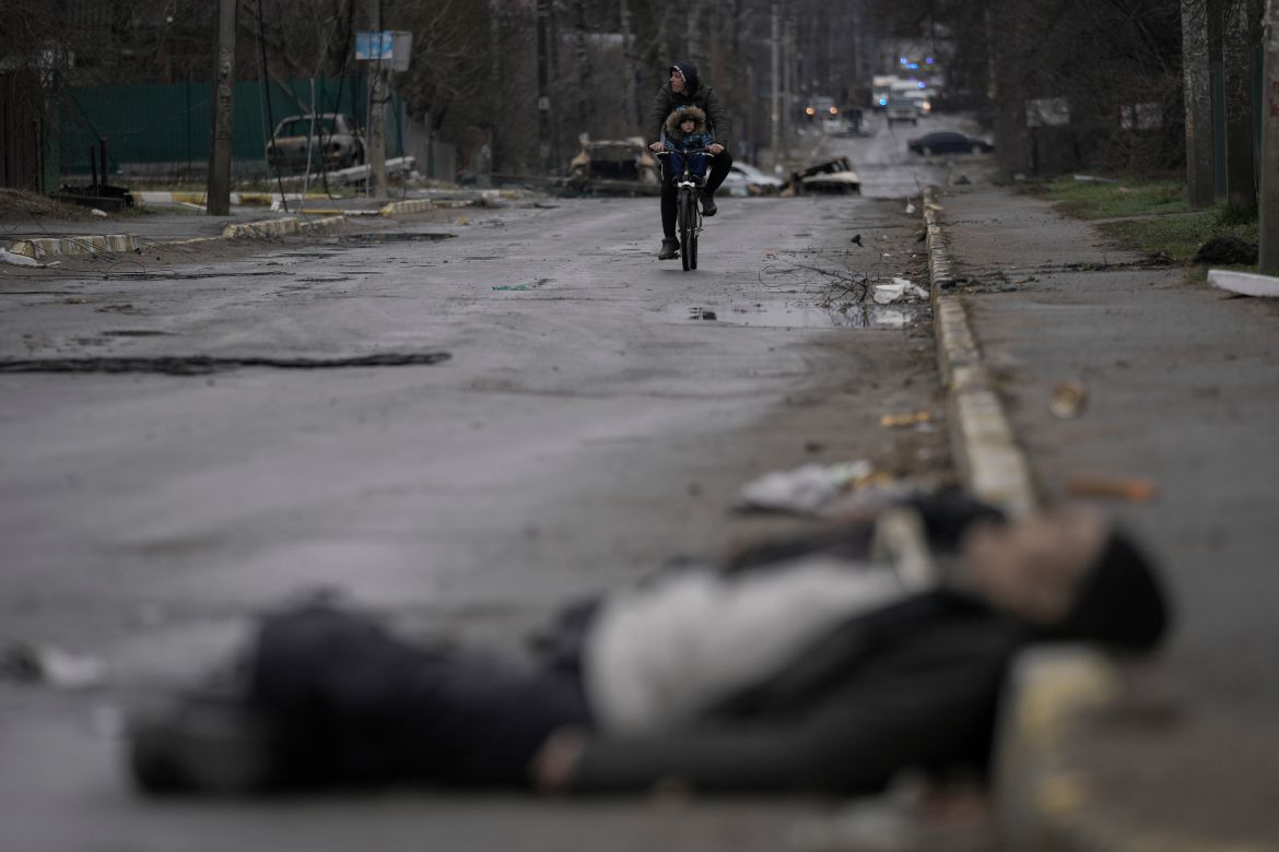 A man and child ride a bicycle as bodies of civilians lie in the street in the formerly Russian-occupied Kyiv suburb of Bucha