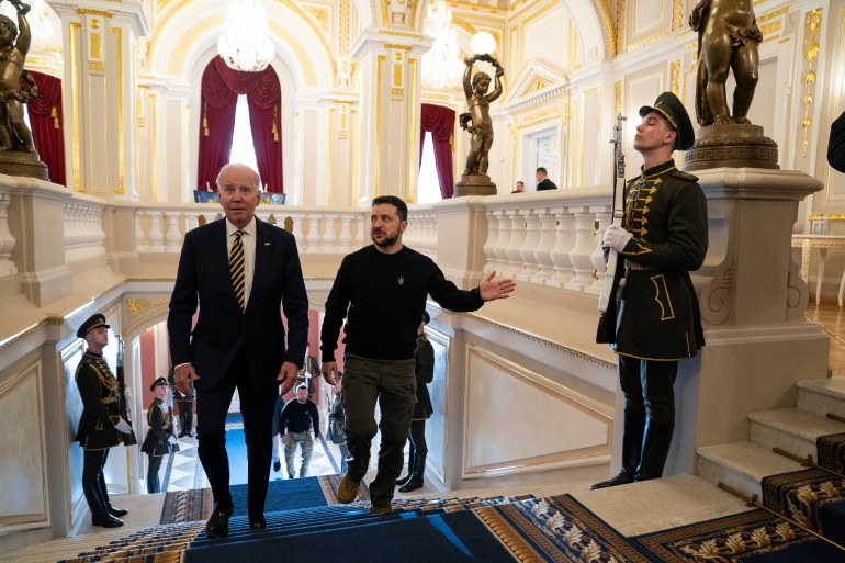 Biden with Zelenskyy going up the stairs at Mariinsky Palace in Kyiv, Ukraine. Ukrainian honour guards holding rifles are posted along the steps.