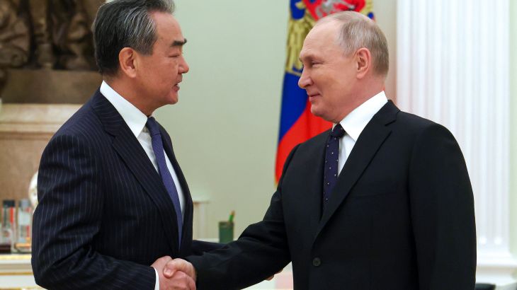 Wang Yi (left) and Vladimiri Putin (right) shake hands as they meet in the Kremlin. There is a flag behind Putin