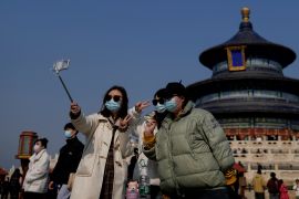 Women wearing face masks take selfies together at the Temple of Heaven park in Beijing, China. It is a sunny February day and the sky is blue.