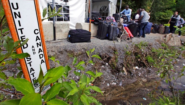 Migrants wait with their luggage outside of a makeshift police station near the US-Canada border