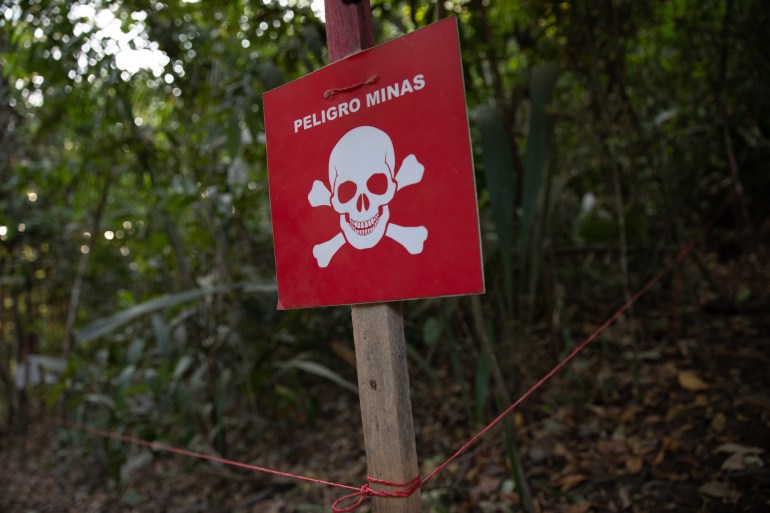 A read sign that reads, in Spanish, "Danger: Mines" sits outside a forested area.