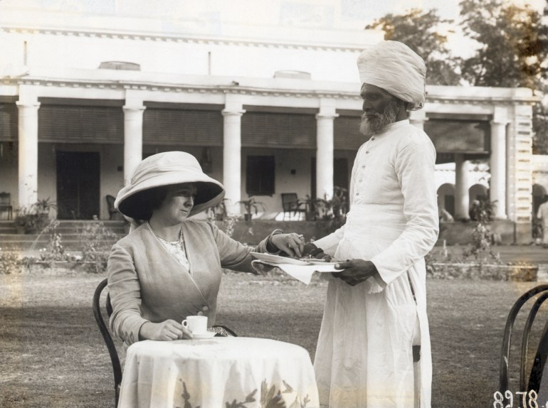 A European woman taking tea from a tray held out to her by an Indian servant