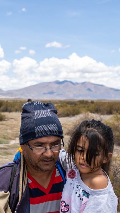 A man carries a young girl in his arms across a desert highland