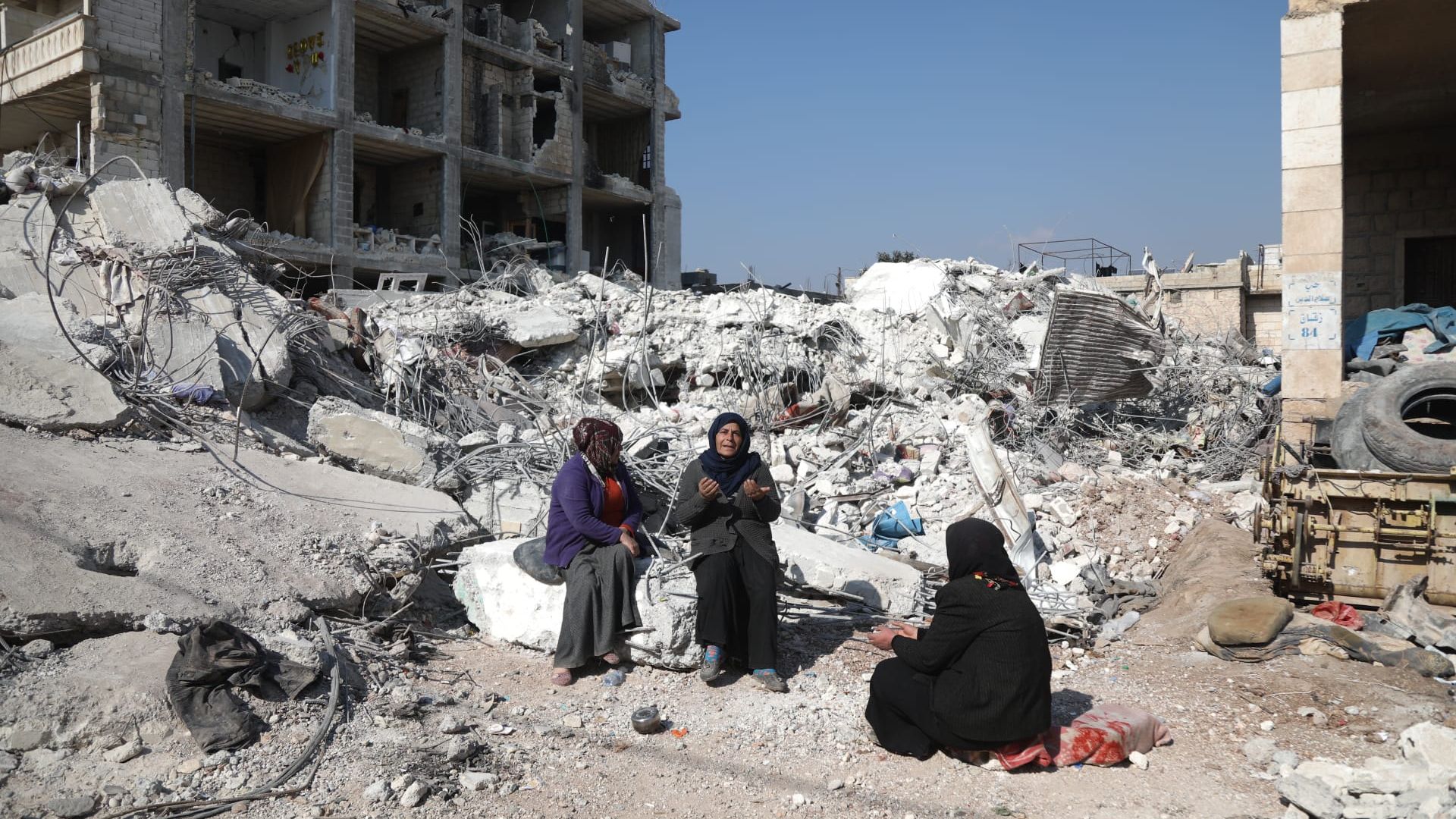 Asmaa' Kousa holds her hands up in prayer as she sits atop the rubble of her home.