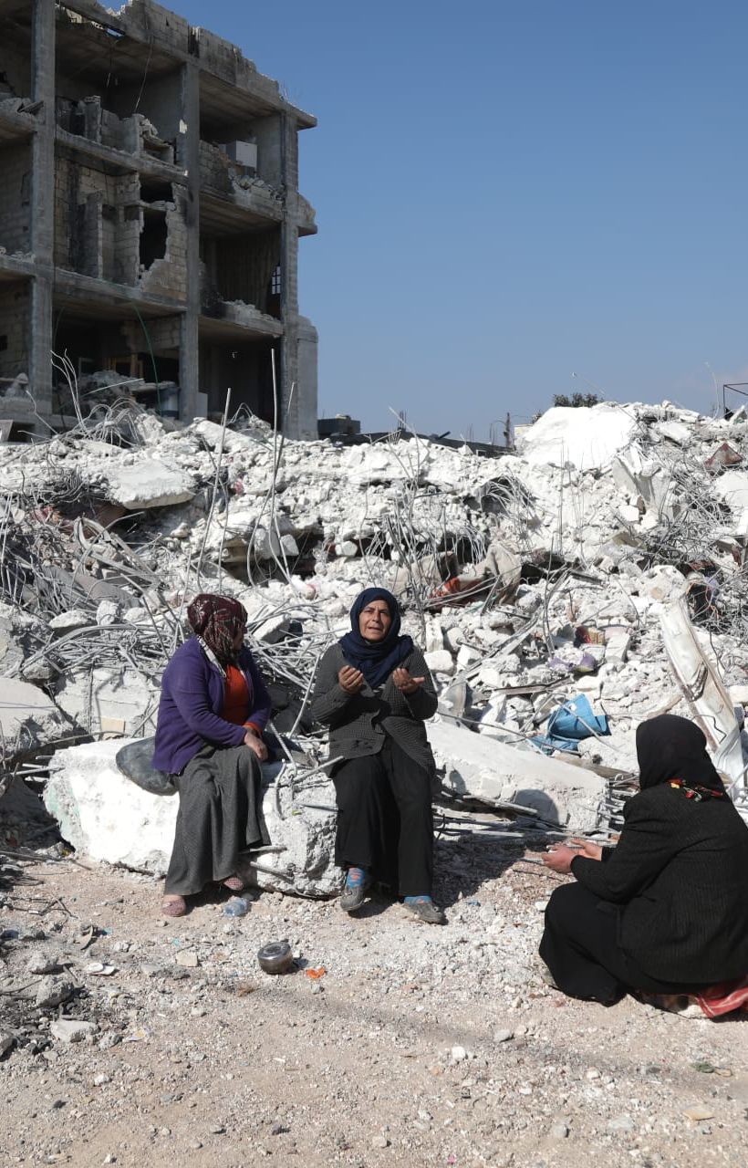Asmaa' Kousa holds her hands up in prayer as she sits atop the rubble of her home.