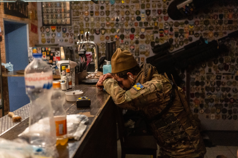 A Ukrainian soldier rests his head on a bar table.
