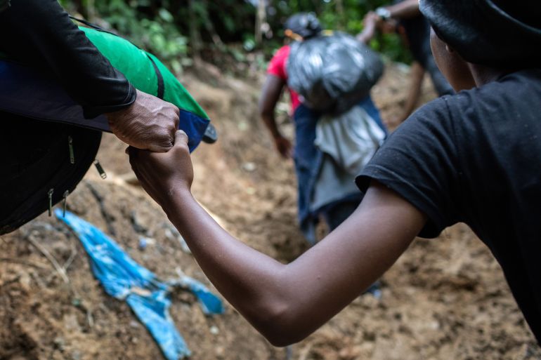 A Colombian guide helps a Haitian woman up a steep mountain slope near Colombia's border with Panama on October 20, 2021 in the Darien Gap, Colombia.