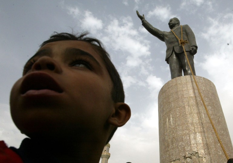 A young Iraqi stands in front of a statue of Iraq's President Saddam Hussein with a noose around its neck
