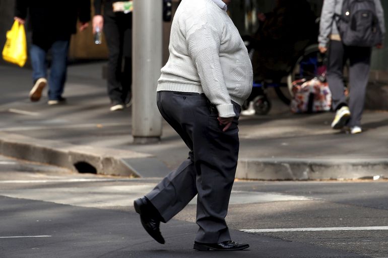 A man crosses a road as pedestrians carrying food walk along the footpath in central Sydney, Australia