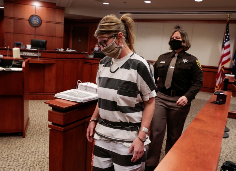 A woman in a striped jump suit is escorted through court by law enforcement