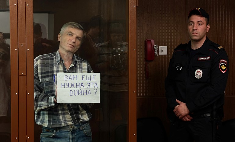 Moscow Councillor Alexei Gorinov, accused of "disseminating clearly false information about Russia's army", holds a placard reading "Do you still need this war?" as he stands inside a defendants' cage during a court hearing in Moscow, Russia July 8, 2022. REUTERS/Stringer